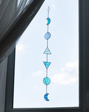 Decorative glass hanging with blue and green shapes in front of a window