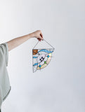 Hand holding a colorful stained glass panel against a white background