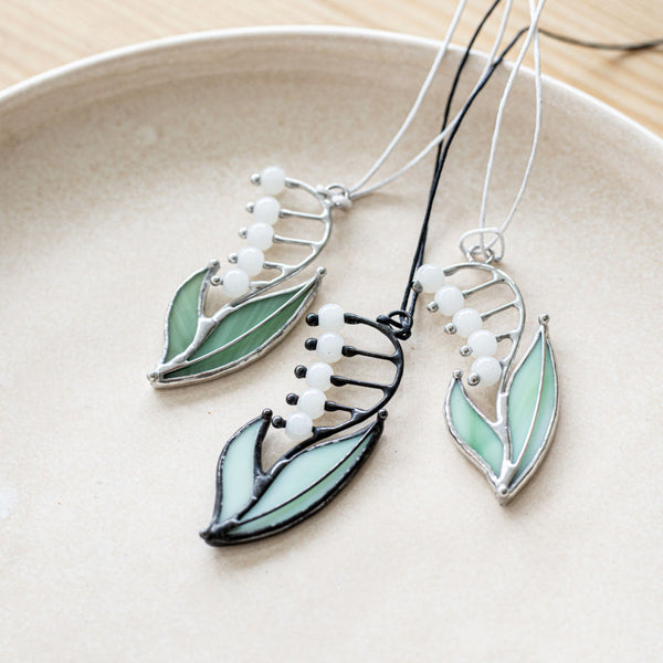 A handcrafted stained glass pendant featuring a patinated copper frame with a geometric pattern, displayed on a plate.